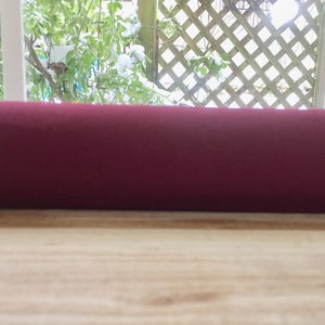 May include: A close-up of a rolled-up burgundy yoga mat on a light wood surface.