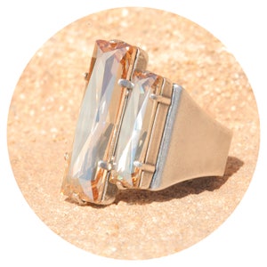 Puede incluir: Un anillo de plata con dos grandes cristales rectangulares de color marrón claro. Los cristales están engastados en una banda de plata y tienen un diseño facetado.