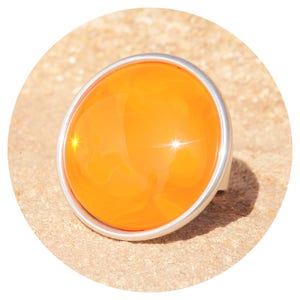 Könnte beinhalten: Ein silberner Ring mit einem großen, runden, orangefarbenen Glasstein.