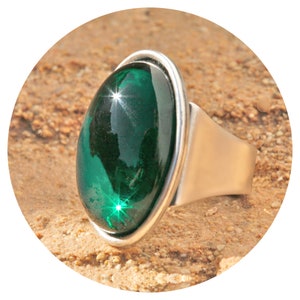 Könnte beinhalten: Ein silberner Ring mit einem großen, ovalen, dunkelgrünen Edelstein. Der Edelstein ist facettiert und reflektiert Licht.