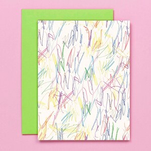 May include: A rectangular greeting card with a white surface covered in colourful scribbles in blue, green, yellow, and red. A bright green envelope is behind the card, set against a pink background.