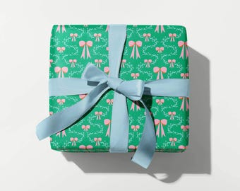 Op de afbeelding: Een groene cadeaudoos met een roze strikpatroon, ingepakt met een lichtblauw lint. De doos is vastgebonden met een strik.
