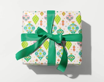 Op de afbeelding: Een witte cadeaudoos met een groen lint en een kleurrijk kerstversieringspatroon. De ornamenten zijn in tinten roze, blauw, groen, geel en oranje.