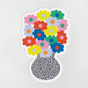 Op de afbeelding: Een boeket kleurrijke bloemen in een zwart-wit gepatroneerde vaas. De bloemen zijn roze, geel, blauw, rood en groen.