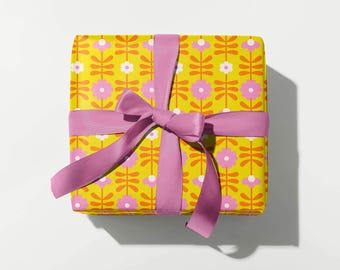 May include: A wrapped gift box with a yellow floral pattern and a pink ribbon tied in a bow. The gift wrap features a repeating pattern of pink flowers and orange stems on a yellow background.