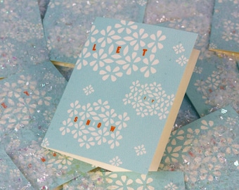Puede incluir: Una tarjeta azul claro con un patrón de copo de nieve blanco y el texto "Let it snow" en letras naranjas.
