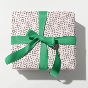 May include: A wrapped gift box with a white and black wavy pattern, tied with a bright green satin ribbon and bow. The gift box is square and sits on a white surface, casting a shadow.
