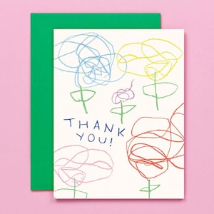 May include: A greeting card with a green envelope and a white card featuring colourful scribbled flower drawings. The words "THANK YOU!" are written in blue. The background is pink.