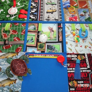 May include: A sports-themed play mat with baseball, football, and golf patterns. Includes a turtle, fish, and toys. Features the text "TOMMY GEAR" and "CHICAGO BLACKHAWKS 1926". Measurements are in centimeters.