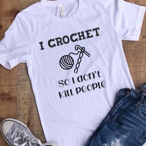 May include: White t-shirt with black text that reads "I crochet so I don't kill people". The text is accompanied by a black and white illustration of a ball of yarn and a crochet hook.