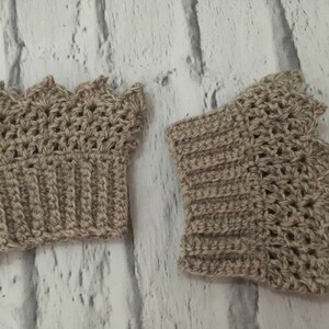 May include: Two crocheted beige wrist warmers with a scalloped edge. The wrist warmers are made with a textured stitch.