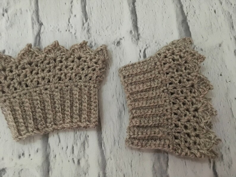 May include: Two crocheted beige wrist warmers with a scalloped edge. The wrist warmers are made with a textured stitch.