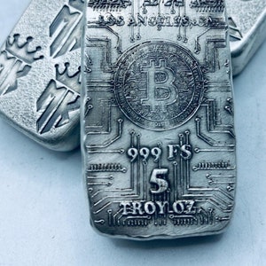Op de afbeelding: Zilveren staaf met Bitcoin-symbool en printplaatontwerp. De staaf is gestempeld met "999 FS", "5 TROY OZ" en "MK Los Angeles, CA". Rechthoekige vorm, matte afwerking.