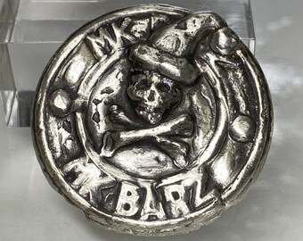 May include: A silver-colored, circular button with a skull wearing a hat and crossed bones. The button has the text "WAKE BARL" around the edge. The design is detailed and slightly raised, giving it a three-dimensional appearance.