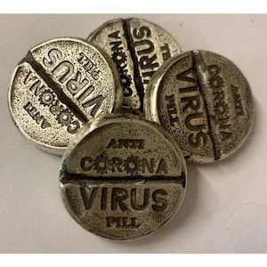 May include: Close-up of four silver-colored, pill-shaped pendants. Each pendant is engraved with the words "ANTI CORONA VIRUS PILL". The pendants have a distressed, vintage appearance, with a split down the middle.