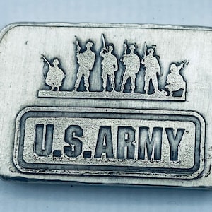 May include: A rectangular silver bar with the words "U.S. ARMY" in a recessed, block-style font. Above the text is a raised relief of soldiers with rifles. The bar has a brushed metal finish.