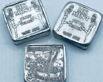 May include: Three silver bars with engraved designs. Two bars feature the text "MK MINT PINUP SERIES" and a pinup girl illustration. The third bar is engraved with the word "JANUARY" and a woman in a bathtub. Each bar is 1 troy ounce of .999 fine silver.