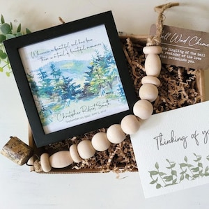 May include: A sympathy gift box containing a framed watercolour painting of trees, a wooden bead garland with a bell, and a card that reads "Thinking of you".