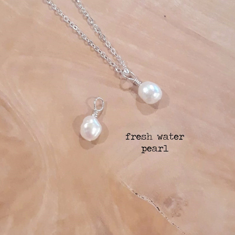 K&ouml;nnte beinhalten: Eine Halskette mit S&uuml;&szlig;wasserperlenanh&auml;nger und ein einzelner Perlenanh&auml;nger. Die Perlen sind wei&szlig; und schillernd, mit einer silbernen Drahtwicklung. Der Text "fresh water pearl" steht darunter.