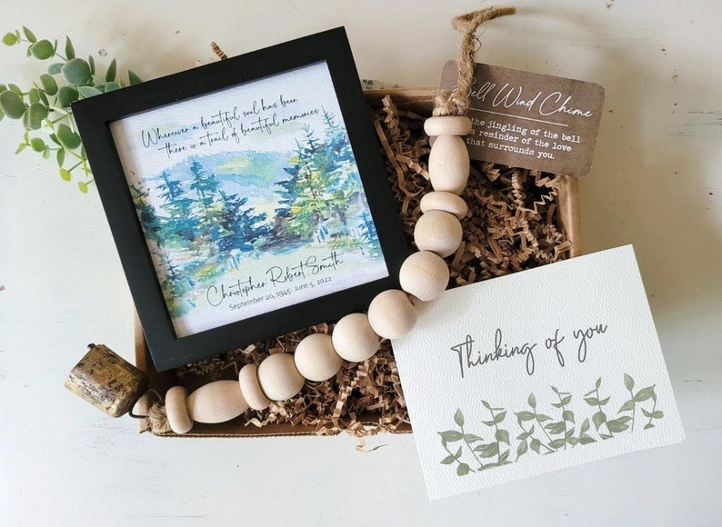 May include: A sympathy gift box containing a framed watercolour painting of trees, a wooden bead garland with a bell, and a card that reads "Thinking of you".