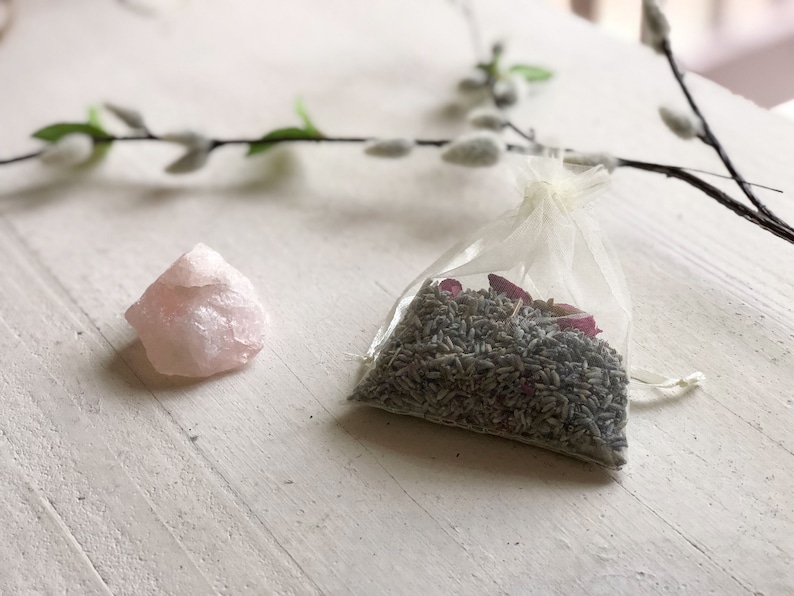 May include: A small pink rose quartz crystal and a white organza bag filled with dried lavender and rose petals.