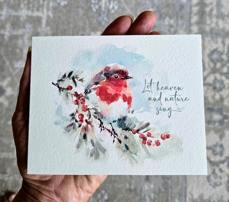 May include: Watercolor greeting card featuring a red-breasted robin perched on a branch with red berries. The card has the text "Let heaven and nature sing" in cursive script. The background is a soft blue and white.