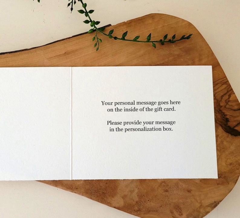 May include: An open white greeting card with text: "Your personal message goes here on the inside of the gift card. Please provide your message in the personalization box." The card is displayed on a wooden board, with greenery in the background.