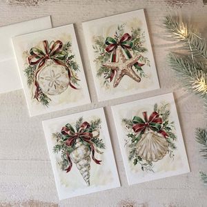 May include: Set of four watercolor Christmas cards featuring marine life designs. Each card showcases a different seashell or starfish, adorned with a red and green bow and festive greenery. The cards are on a cream-colored background.