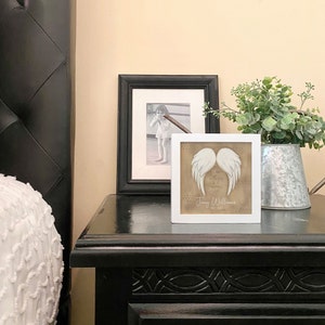 May include: White framed picture with a beige background and white angel wings. The text reads "I know that you are always with me" and "Jenny Williams 1952-2023".