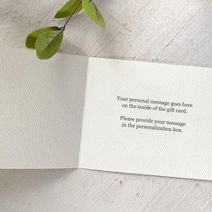 K&ouml;nnte beinhalten: Eine offene, wei&szlig;e Geschenkkarte mit dem Text "Your personal message goes here on the inside of the gift card. Please provide your message in the personalization box." Ein Zweig mit gr&uuml;nen Bl&auml;ttern befindet sich im Hintergrund.