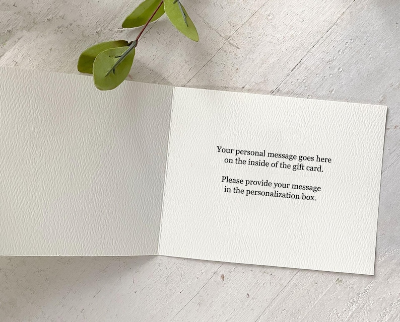 K&ouml;nnte beinhalten: Eine offene, wei&szlig;e Geschenkkarte mit dem Text "Your personal message goes here on the inside of the gift card. Please provide your message in the personalization box." Ein Zweig mit gr&uuml;nen Bl&auml;ttern befindet sich im Hintergrund.