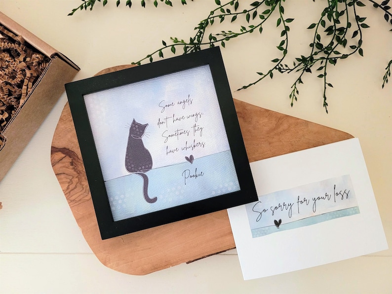 May include: A black framed print featuring a cat illustration and the text "Some angels don't have wings. Sometimes they have whiskers. Pookie." A card with the text "So sorry for your loss" is also present.