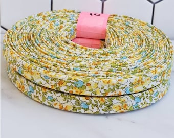 May include: A roll of white fabric ribbon with a yellow and blue floral print. The ribbon is approximately 10 yards long.