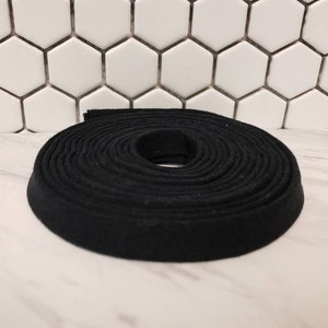 May include: A black fabric trim, rolled up in a coil, ready for sewing or crafting projects.