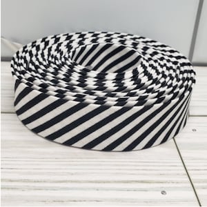 May include: A roll of black and white striped fabric ribbon. The ribbon is rolled up tightly and the stripes are diagonal.
