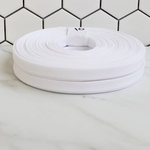 May include: A white roll of double fold bias tape with a label that says "1/2".