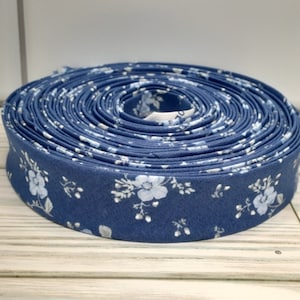 May include: A roll of blue and white floral fabric trim. The trim is a thin, flat ribbon with a repeating pattern of small white flowers on a blue background.