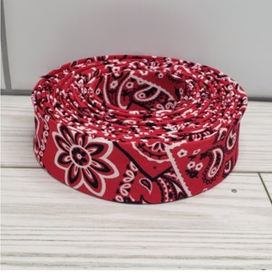 May include: A roll of red and white bandana print fabric ribbon. The ribbon is rolled up and the bandana print is visible on the outside of the roll.
