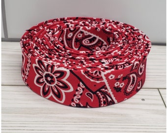 May include: A roll of red and white bandana print fabric ribbon. The ribbon is rolled up and the bandana print is visible on the outside of the roll.