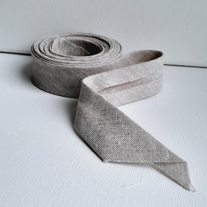 May include: A roll of natural linen ribbon with a raw edge. The ribbon is folded in half and the ends are pointed.