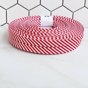 May include: A roll of red and white striped ribbon. The ribbon is approximately 1 inch wide and is wound into a circle. The ribbon is on a white surface.
