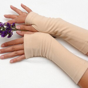 May include: A pair of beige fingerless gloves with a ribbed texture. The gloves are made of a soft, stretchy fabric and are worn on both hands.