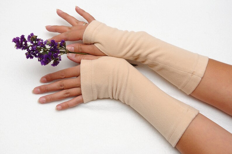 May include: A pair of beige fingerless gloves with a ribbed texture. The gloves are made of a soft, stretchy fabric and are worn on both hands.