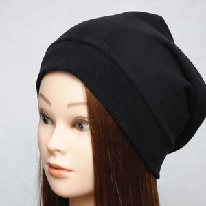 May include: A black beanie hat made of soft fabric. The hat is slouchy and has a fold-over brim.