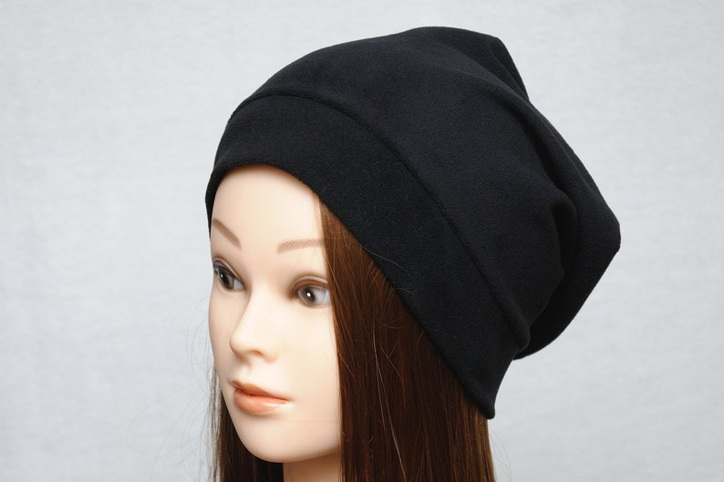 May include: A black beanie hat made of soft fabric. The hat is slouchy and has a fold-over brim.