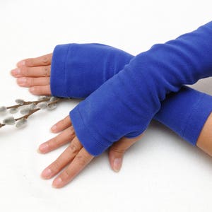 May include: A pair of blue fleece arm warmers. The arm warmers are folded over each other and are being held by a person's hands.
