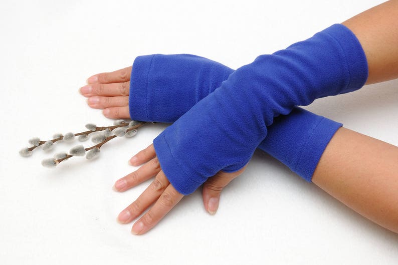 May include: A pair of blue fleece arm warmers. The arm warmers are folded over each other and are being held by a person's hands.