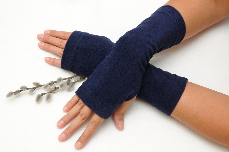May include: A pair of navy blue fleece fingerless gloves. The gloves are folded over each other and are lying on a white surface.