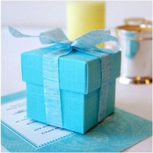May include: A small, light blue gift box with a satin ribbon tied around it. The box is sitting on a patterned surface.