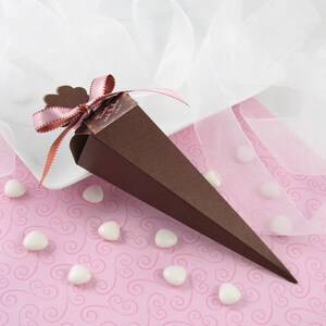 May include: A brown cone-shaped favor box with a pink ribbon and a small heart-shaped tag. The tag has the text "Brenda and John" on it. The box is sitting on a pink background with white hearts.
